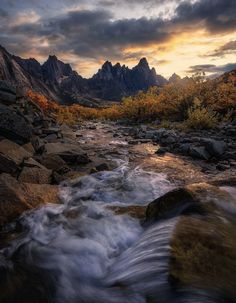 a river running through a rocky valley under a cloudy sky with mountains in the background