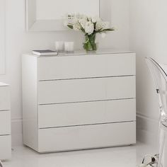 a white dresser sitting next to a mirror in a room with flowers on top of it