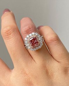 a close up of a person's hand holding a ring with a red and white diamond