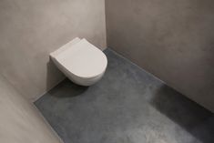 a white toilet sitting in a bathroom next to a gray wall and cement flooring