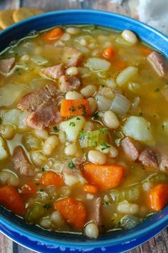 a bowl of soup with ham, beans and carrots in it on a wooden table