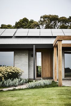 a modern house with solar panels on the roof and windows, grass in front of it