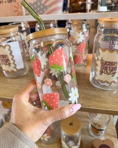 a person holding a strawberries and daisies in a mason jar with stickers on it