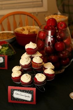 a table topped with cupcakes covered in frosting next to apples and other food