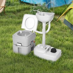 a toilet and sink in the grass next to a tent with camping equipment on it