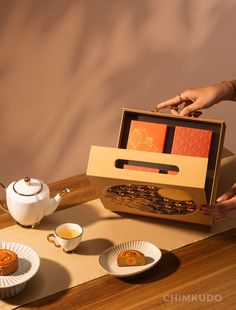 a person holding a box with food in it on top of a table next to plates and cups