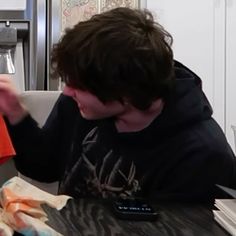 a young man sitting at a table with an orange shirt in front of his face