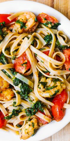 pasta with shrimp, tomatoes and spinach in a white bowl on a wooden table