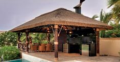 a gazebo with an outdoor kitchen next to a pool in the middle of a tropical setting