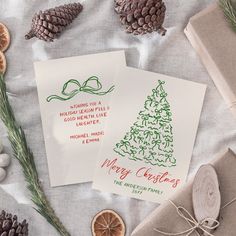 two christmas cards sitting on top of a table next to pine cones and other decorations