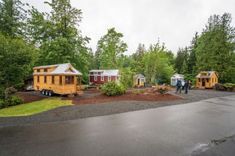 several tiny houses in the middle of a lot with people walking around them and trees