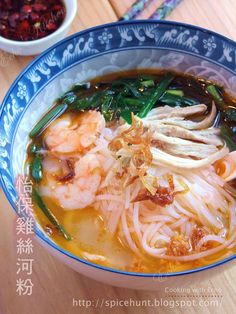 a bowl of soup with shrimp, noodles and greens in it on a wooden table