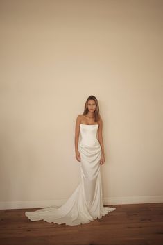 a woman standing in front of a wall wearing a white dress