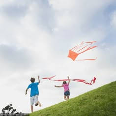 two people are flying kites on a grassy hill