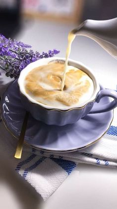 a person pouring milk into a cup on top of a blue saucer with lavender flowers in the background