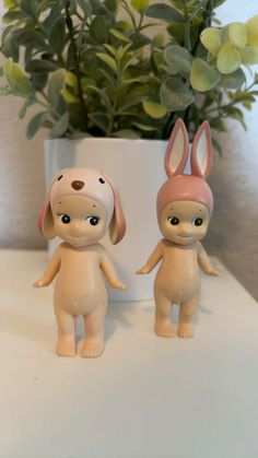 two small toy animals standing next to each other on a table near a potted plant