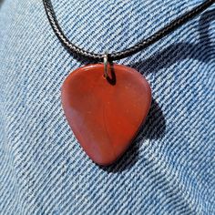 a red heart shaped pendant hangs from a black leather cord on a blue jean shirt