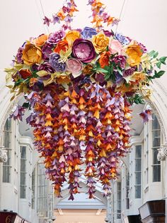 an arch made out of paper flowers and leaves in front of a building with arched windows