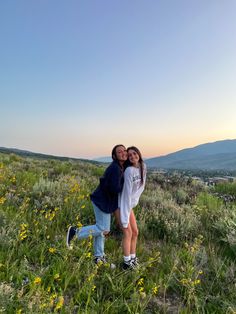 two girls are standing in a field with wildflowers and mountains in the background