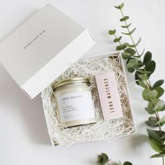 an open box with a candle and some green leaves next to it on a white surface