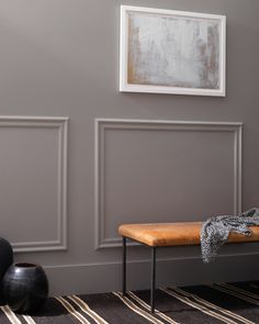 a wooden bench sitting in front of a gray wall with white paneling on it