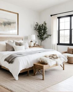 a bedroom with white bedding, pillows and fur rugs on the floor next to a large window