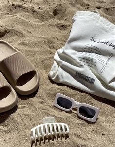 a pair of sandals, sunglasses and comb laying on the sand next to a towel