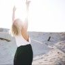 a woman standing on the beach with her arms in the air