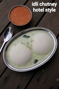 two bowls of food sitting on top of a wooden table next to spoons and sauce