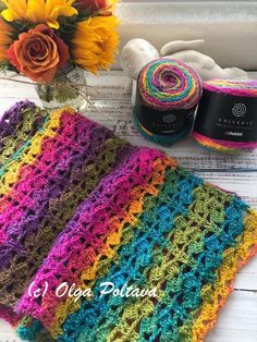 a crocheted blanket and some yarn next to a vase with sunflowers