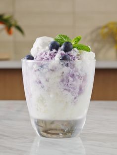 a dessert with blueberries and ice cream in a glass bowl on a counter top