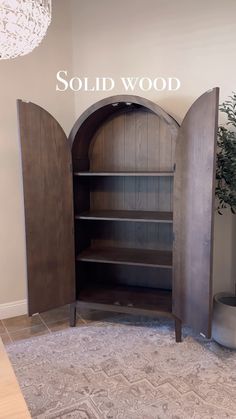 an arched wooden bookcase in the corner of a room with a potted plant