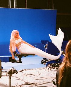 a woman with long pink hair laying on a bed in front of a blue screen