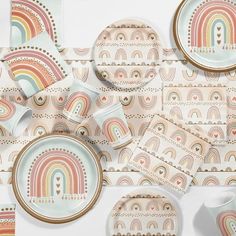 an assortment of colorful plates and cups on a tablecloth with rainbows in the background