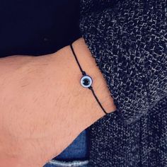 a man wearing a black cord bracelet with an evil eye charm on his left wrist