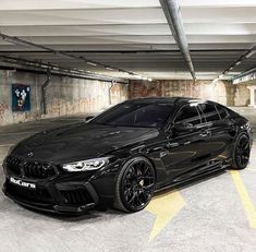 a black bmw is parked in a parking garage with yellow lines on the floor and walls