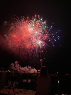 a person sitting on a dock watching fireworks