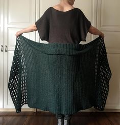 a woman holding up a green knitted shawl in front of white closet doors