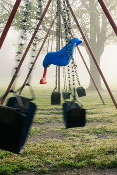 a blue horse on a swing set in a park with foggy trees behind it