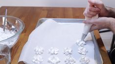 a person is decorating cupcakes with icing on a baking sheet in front of a glass bowl