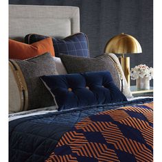 a bed with blue and orange pillows on top of it next to a gold lamp