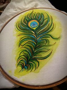 a peacock feather is painted on a yellow background in a wooden hoop with white fabric