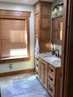 a bathroom with wooden cabinets and marble counter tops, along with a large window in the corner