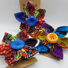 two colorful hair clips with buttons on them sitting next to each other in front of a cardboard box