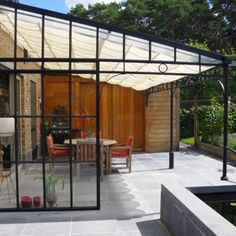 an outdoor dining area with glass walls and patio furniture in the foreground, next to a pond