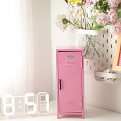 a pink locker sitting on top of a white table next to a vase with flowers