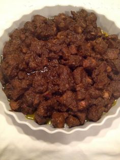 a bowl filled with meat and sauce on top of a white tablecloth covered table