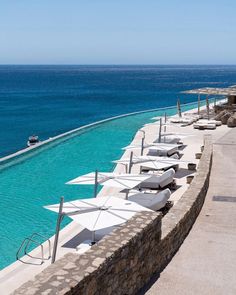 several umbrellas are lined up along the edge of an empty swimming pool with blue water in the background