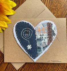 a heart shaped piece of fabric on top of an envelope next to a sunflower