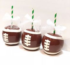 three chocolate covered candy apples with green and white striped straws in football themed cups